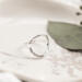 Single open circle sterling silver ring on white marbled dish with green leaf.

